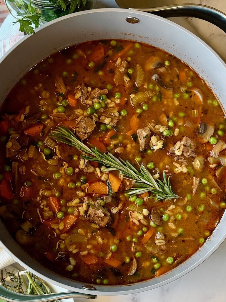 Beef barley stew in a pot with a sprig of fresh rosemary