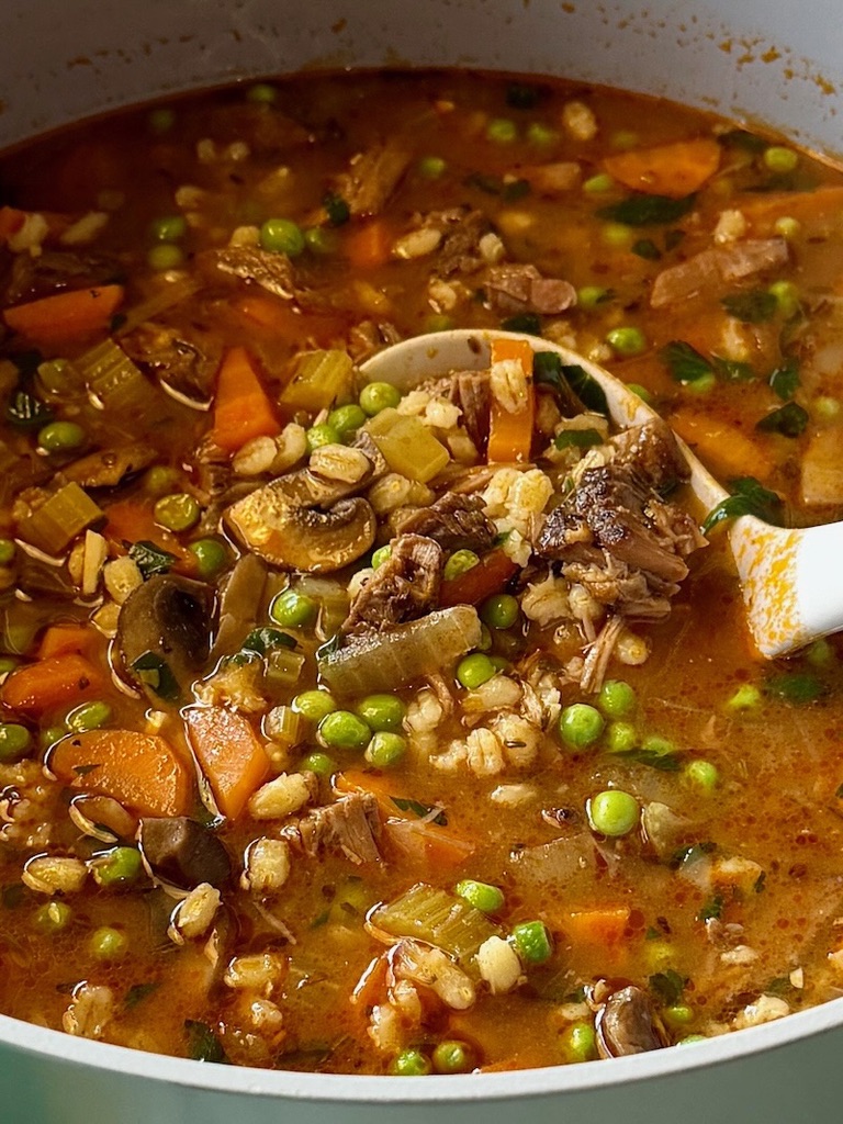 Pot of Beef barley stew with a ladle.