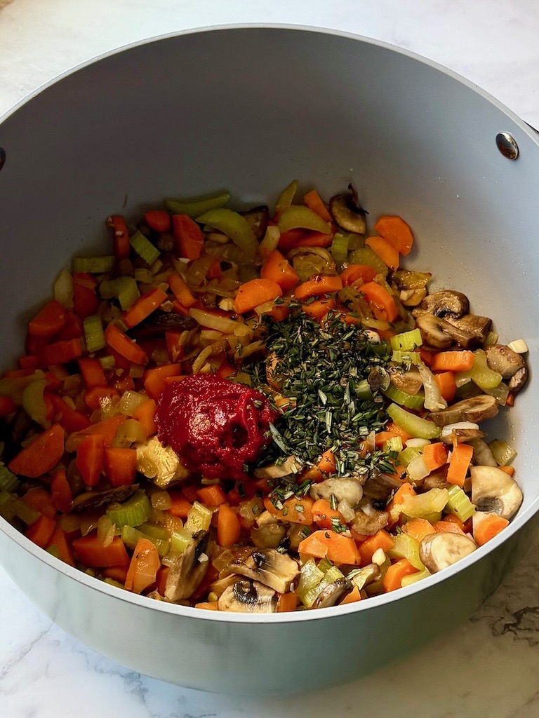 Tomato paste and herbs added to the veggies in the pot.