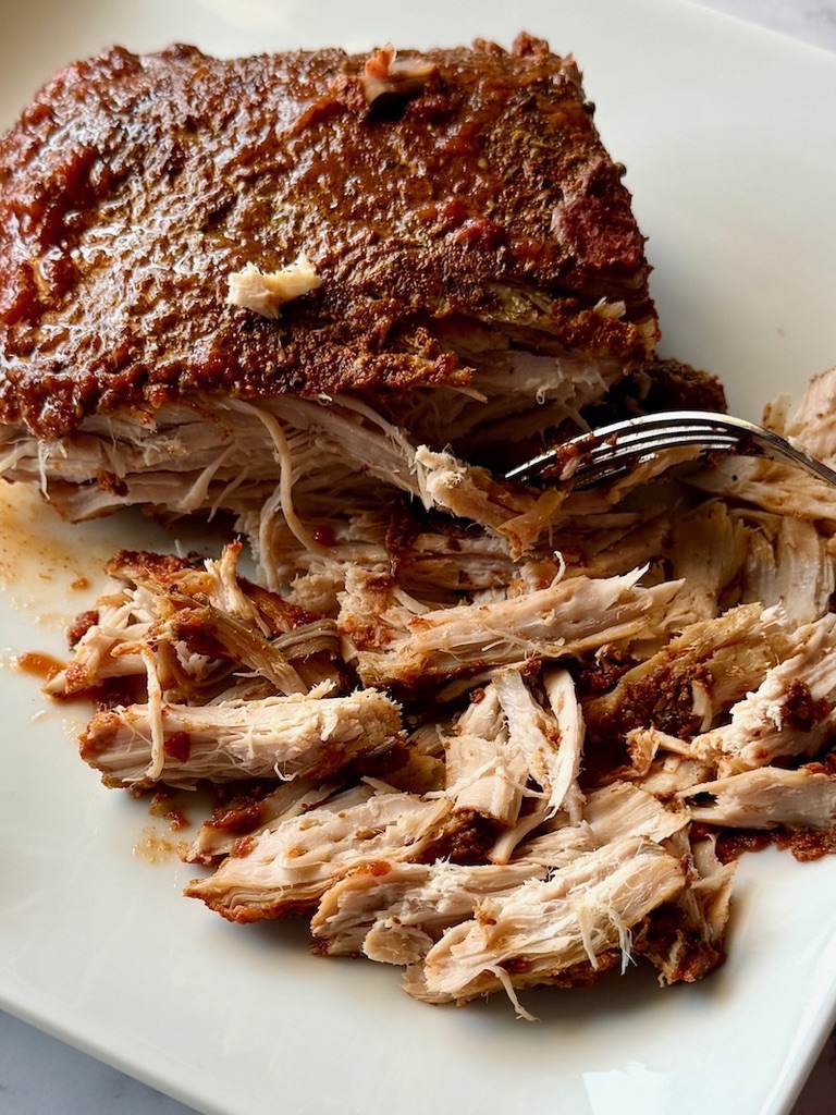 Pork roast on a plate shredded with a fork.