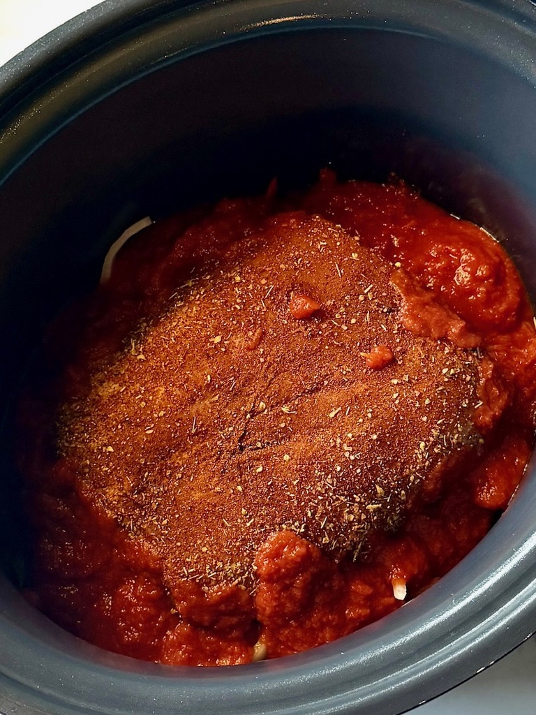 Seasoned pork roast on top of the veggies with fire roasted tomatoes around the pork