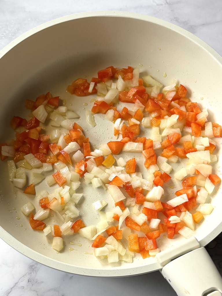Bell peppers and onions sauté in a skillet with olive oil
