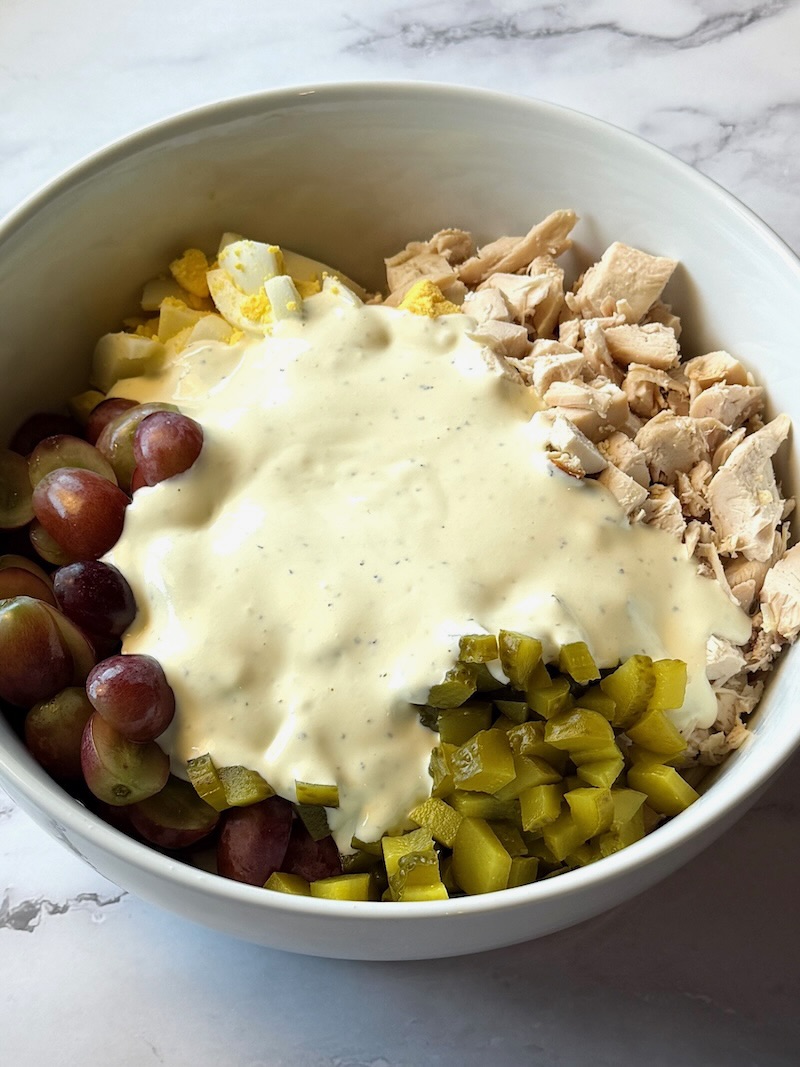 Chicken salad ingredients in a serving bowl with dressing over the top.