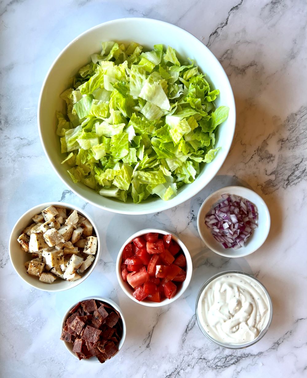 Ingredients list. Lettuce, cooked cubed chicken, cooked bacon, tomatoes, onion, and ranch dressing.