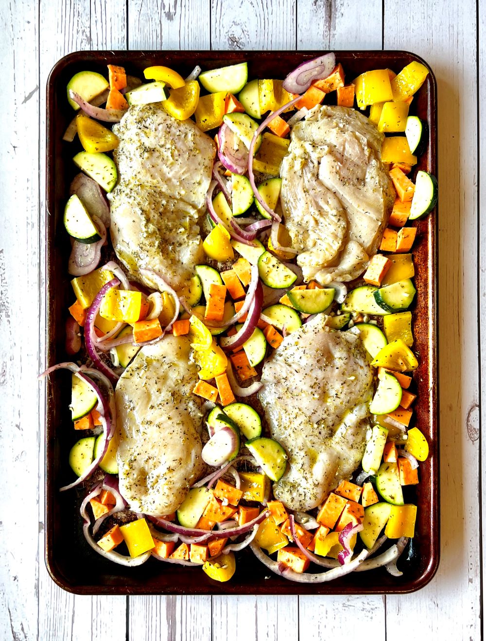 Chicken and veggies assembled on large sheet pan before roasting in the oven. 