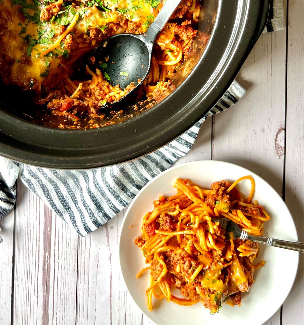 Slow cooker pot with spaghetti casserole and a plate with spaghetti on it