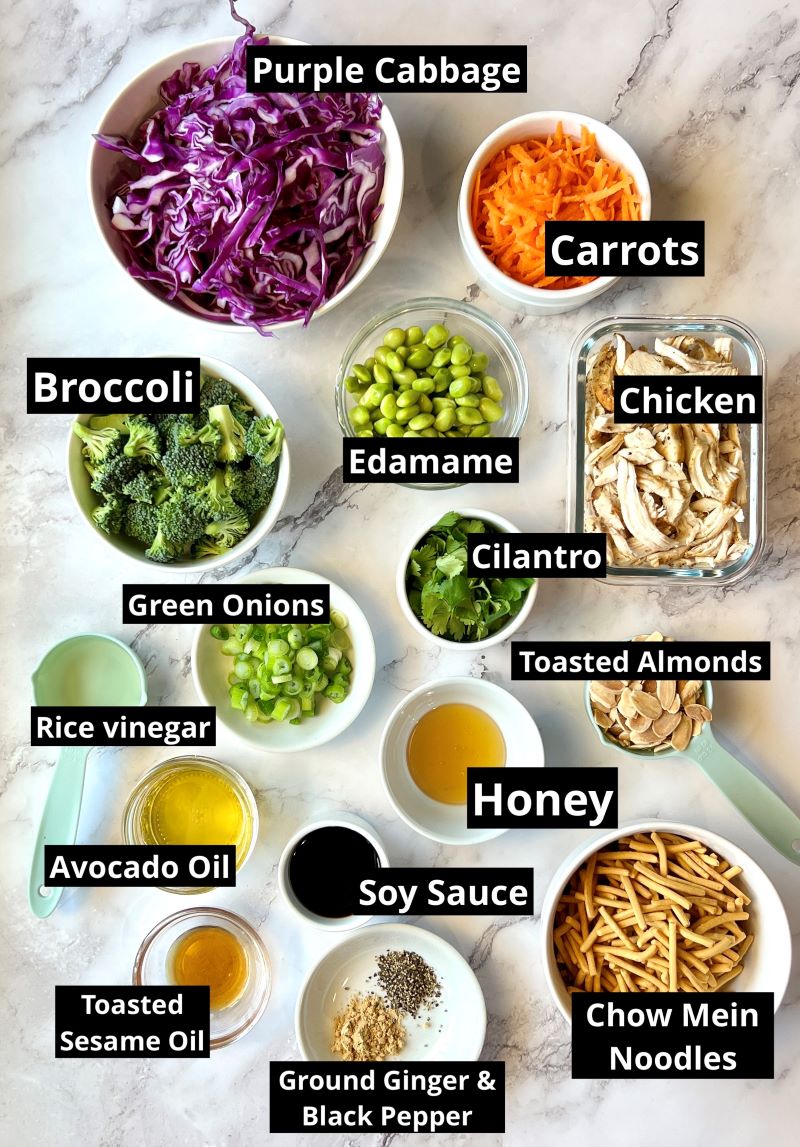 Ingredients for crunchy Asian chopped salad. Purple cabbage, carrots, broccoli, edamame, green onions, chicken, cilantro, rice vinegar, toasted almonds, honey, avocado oil, soy sauce, toasted sesame oil, chow mein noodles, ground ginger, salt and pepper. 
