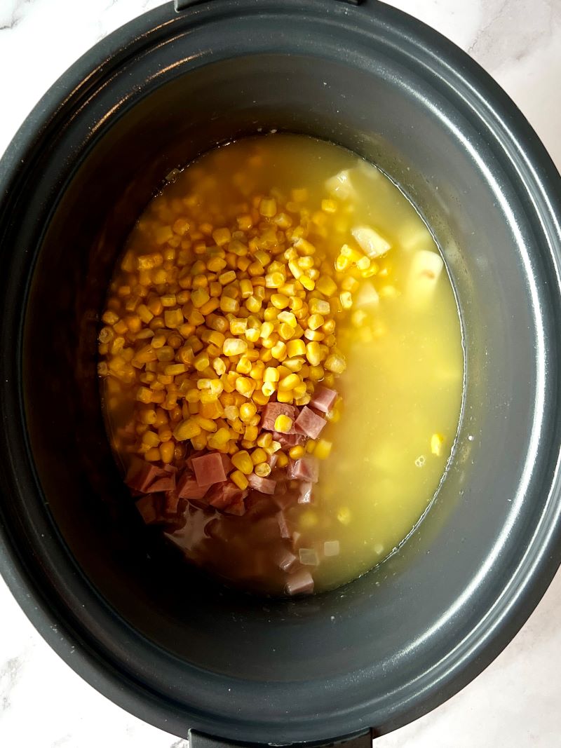 Slow cooker with onions, garlic, potatoes, ham, corn, and chicken broth.