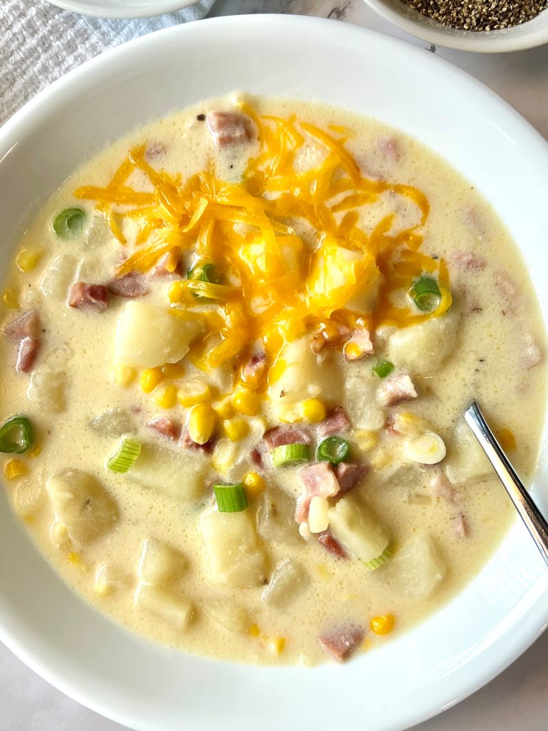 Bowl of cheesy ham and potato chowder with cheese on top and green onions
