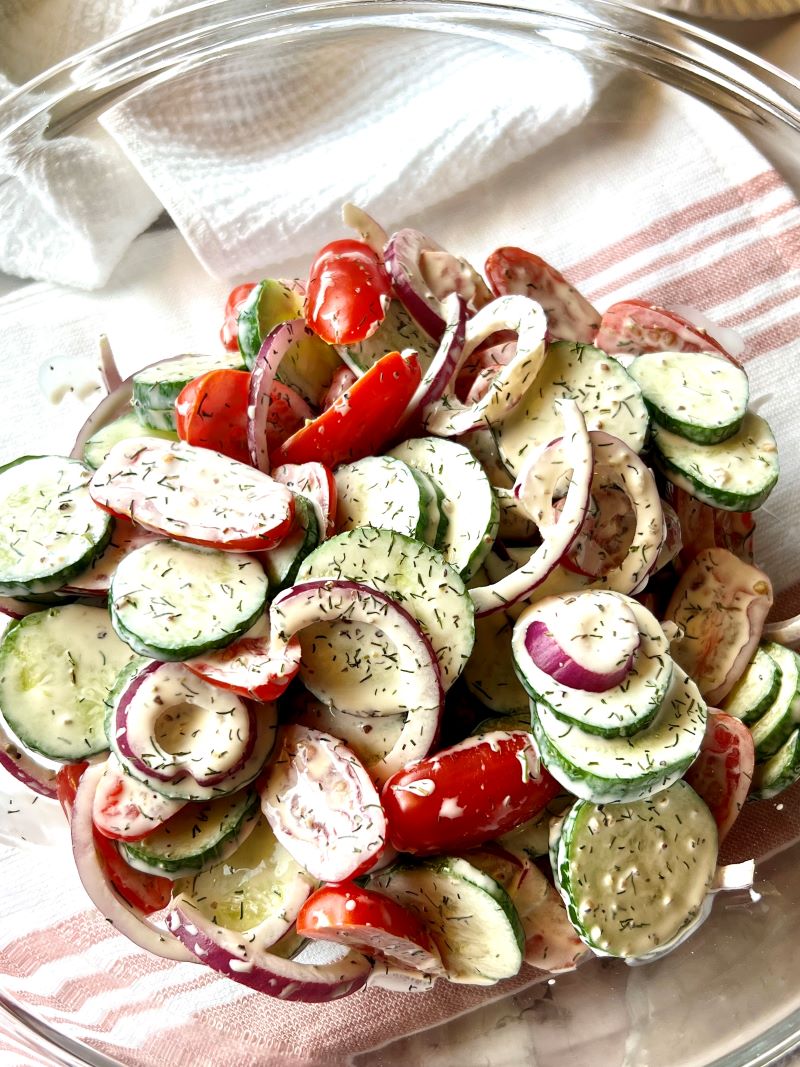 Cucumbers, tomatoes, and red onion combined with dressing in a large bowl.