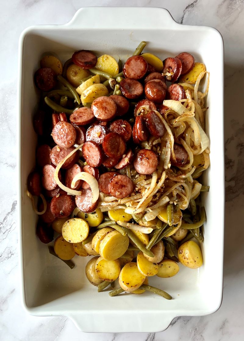 Potatoes, sausage, green beans, and onions added to a casserole dish to bake.