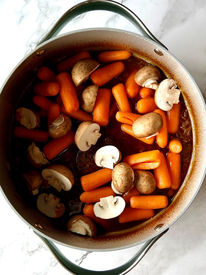 Roast, carrots, mushrooms, beef broth, and wine cooked in a large pot. 