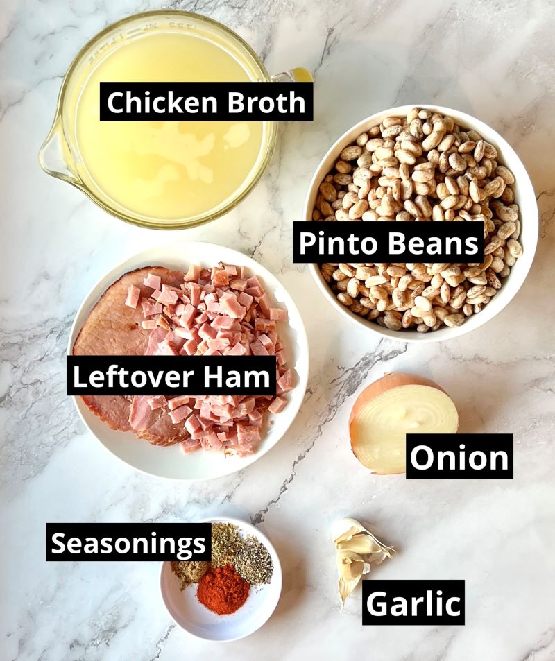 Ingredients for slow cooker pinto beans and ham. Chicken broth, dry pinto beans, ham, onion, garlic, smoked paprika, cumin, oregano, black pepper, bay leaves.