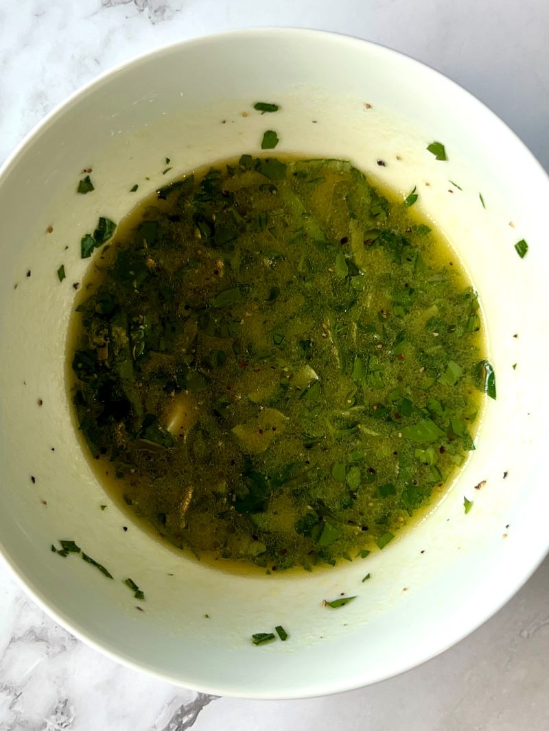 Lemon dressing combined in a small bowl. Olive oil, lemon juice, Dijon mustard, smashed garlic, honey, fresh parsley and basil, salt and pepper.