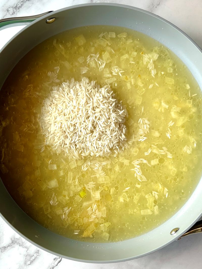 Rice with chicken broth in a skillet.