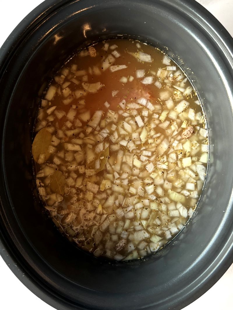 Slow cooking with dried pinto beans, ham, onions, garlic, seasonings, bay leaves, and chicken broth. 