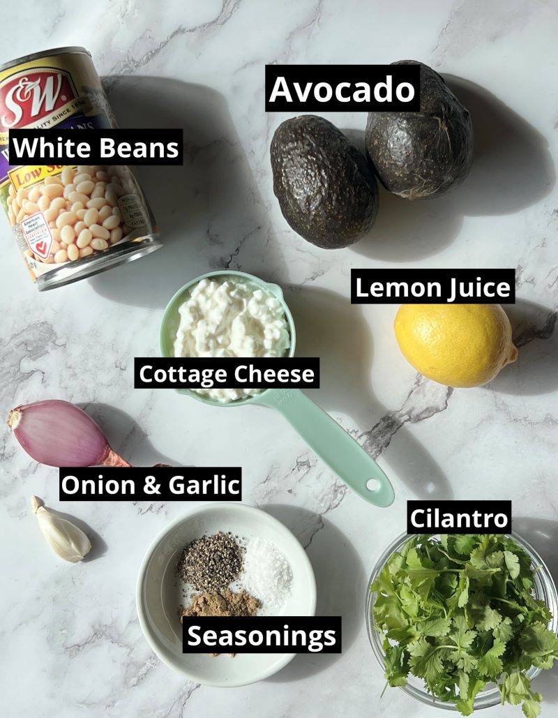 Ingredients for high-protein guacamole dip. White beans, avocado, cottage cheese, lemon juice, onion, garlic, cilantro, cumin, salt and pepper.