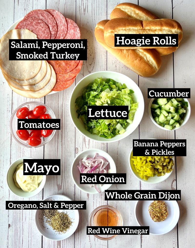 Ingredients displayed on a white board for Italian chopped salad hoagie rolls--meat, hoagie rolls, veggies, and dressing items.