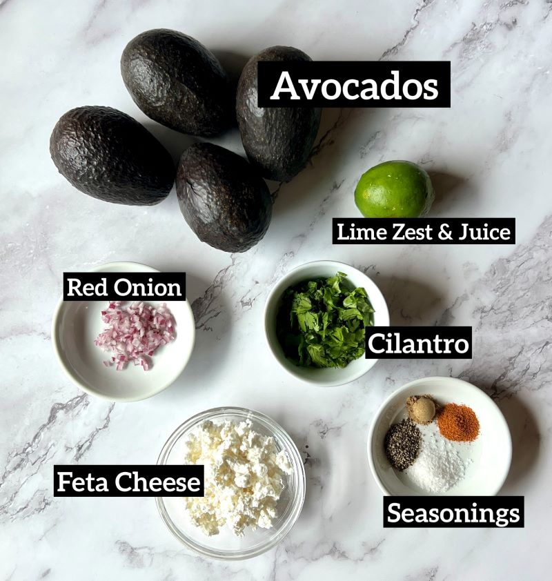 Ingredients set out for guacamole dip with feta. Avocado, lime juice and zest, red onion, cilantro, feta cheese, and seasonings. 
