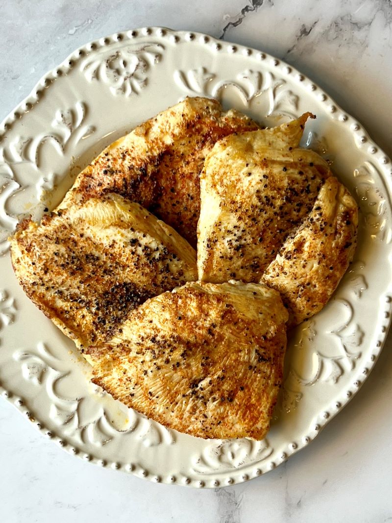 Cooked chicken breast on a plate for chicken Caesar pasta salad.