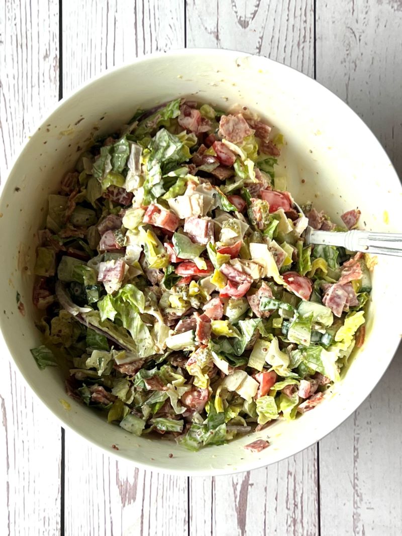 Chopped salad mixed with dressing in a medium bowl.