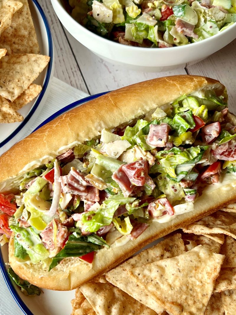 Italian chopped salad prepared and stuffed in soft hoagie rolls with a side of nacho tortilla chips.