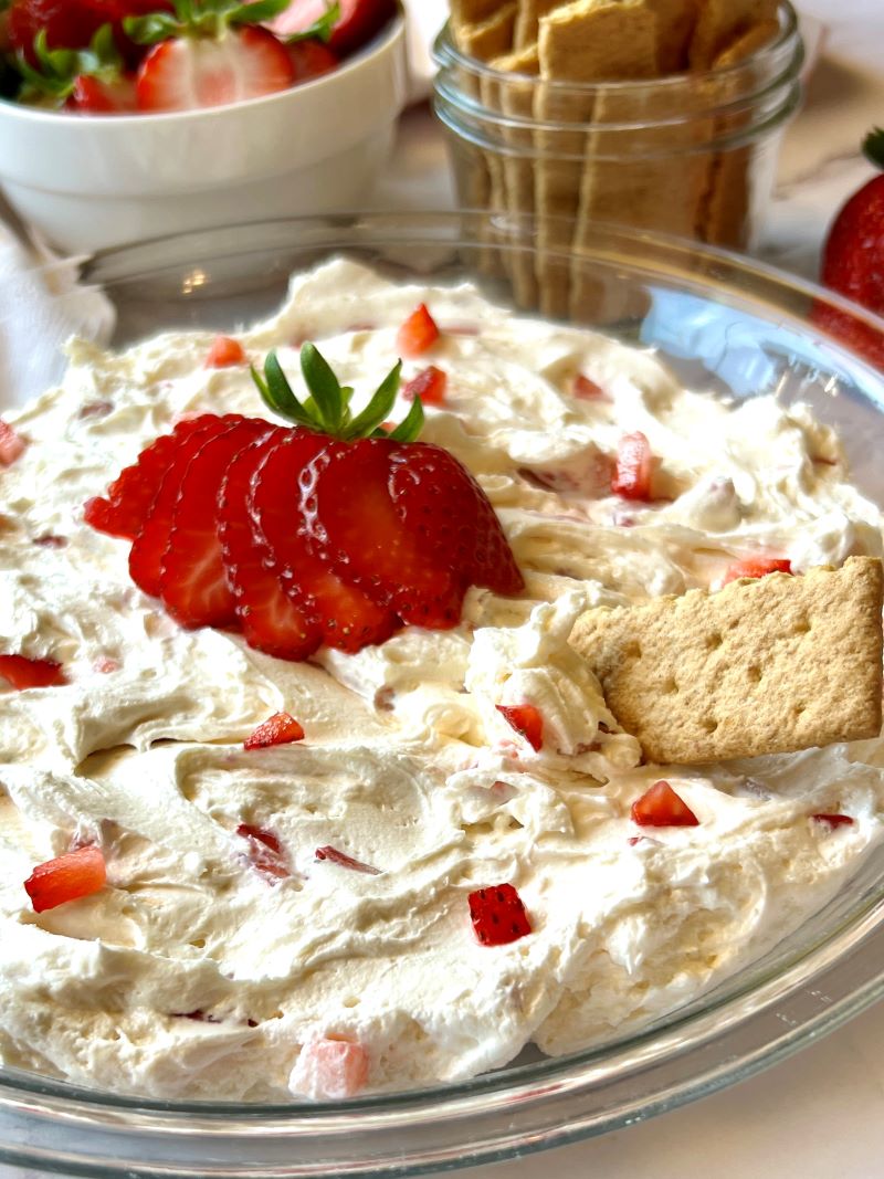 Strawberry cream cheese dip spread in a pie dish and topped with fresh strawberries and a graham cracker.