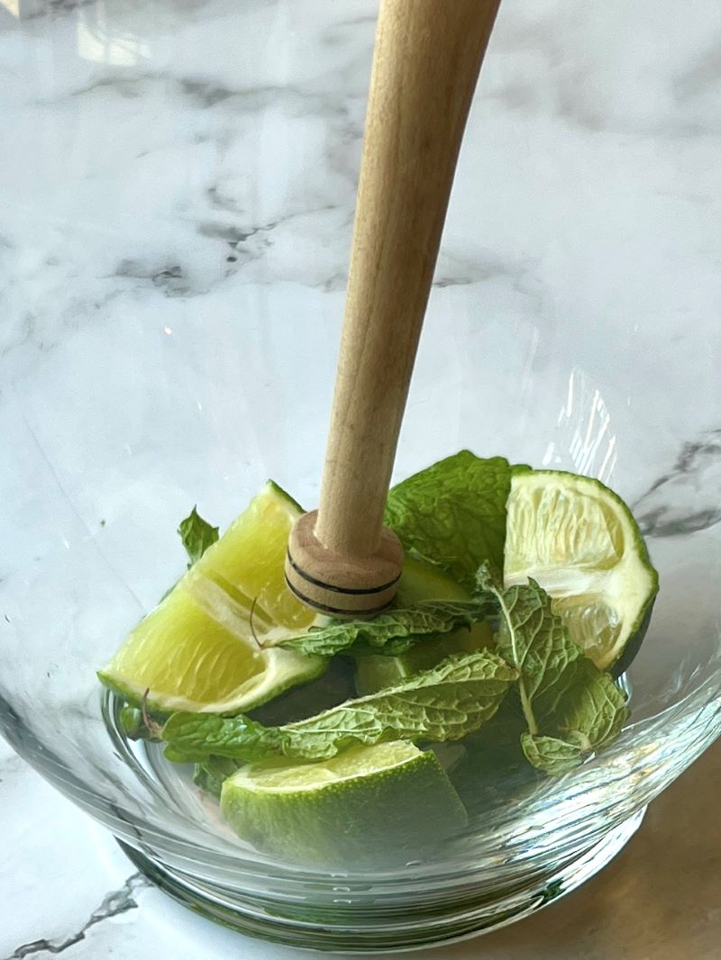 large glass pitcher with fresh mint and lime wedges with a wooden muddler.