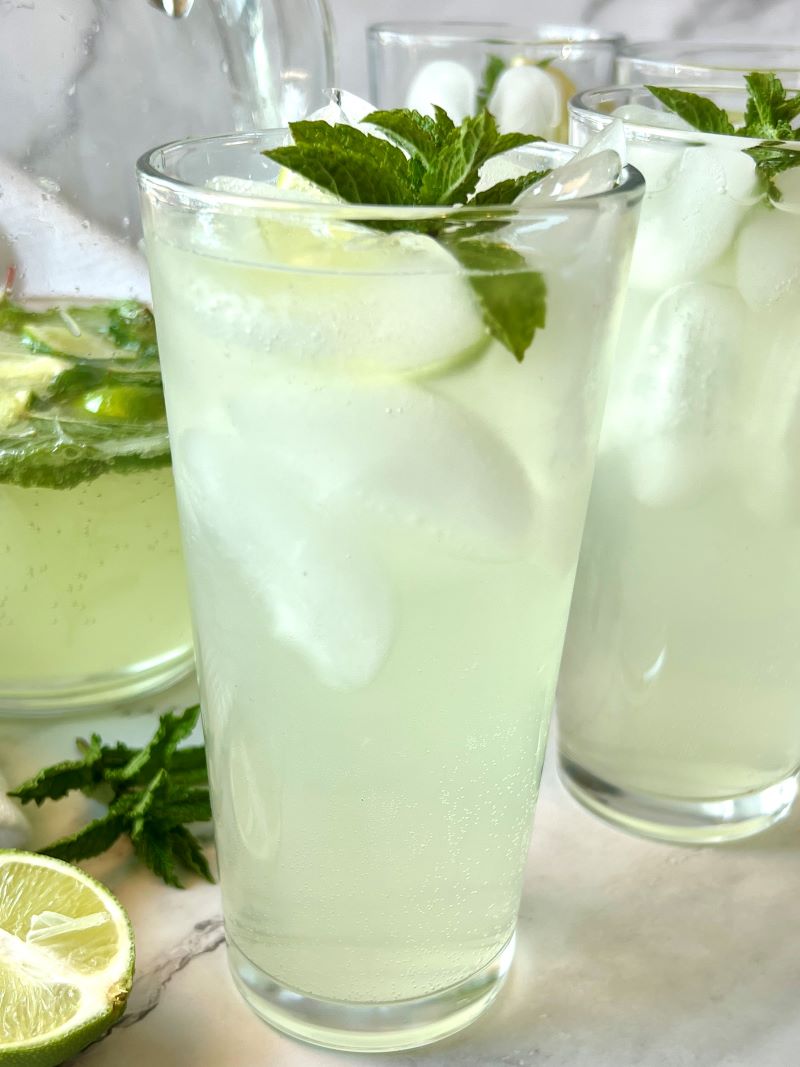 Tall glass filled with ice and mojito mocktail, garnished with mint and lime.