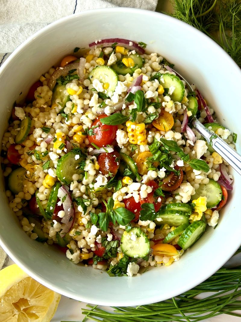 Couscous salad mixed together in a bowl with a spoon. 