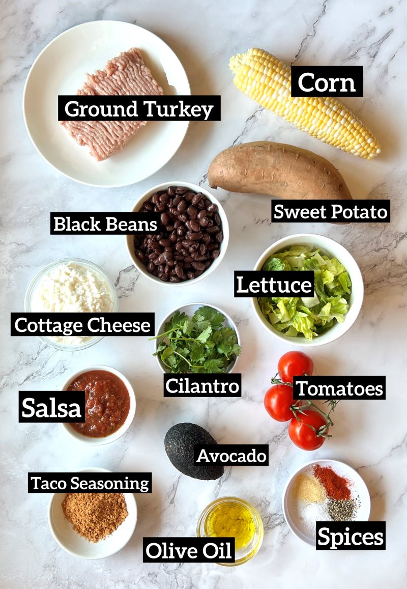 ingredients displayed for ground turkey power bowls. Ground turkey, sweet potato, fresh corn on the cob, black beans, lettuce, cottage cheese, cilantro, tomatoes, salsa, avocado, taco seasoning, olive oil, smoked paprika, garlic powder, salt and pepper. 