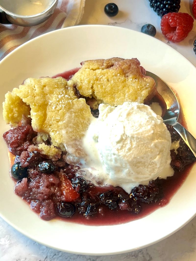 Cooked cobbler in a bowl with ice a scoop of ice cream in a serving bowl.