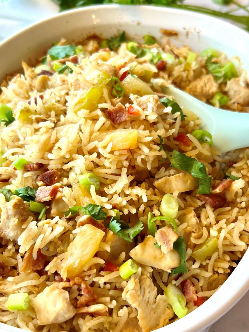 pineapple chicken rice casserole in a dish with a large spoon.