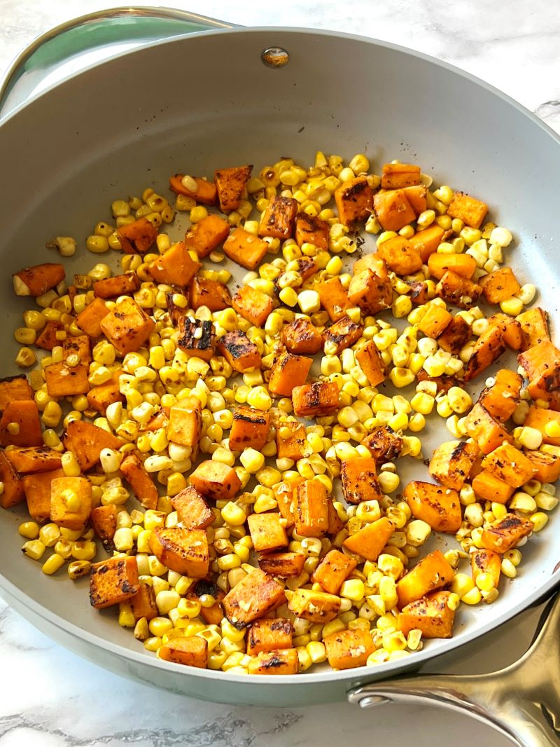 Diced sweet potatoes and fresh corn cooked in a skillet.