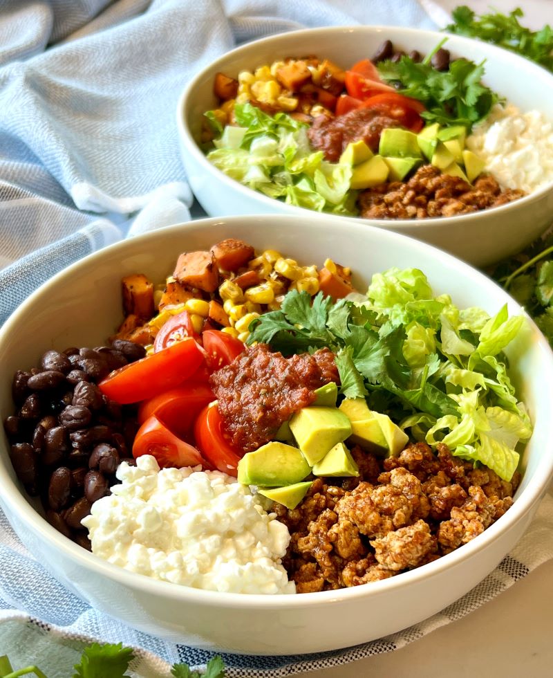 Two ground turkey power bowls assembled with meat, beans, meat, fresh toppings, cottage cheese, and salsa. 
