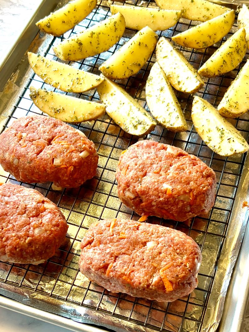 Four mini meatloaves with potato wedges on a sheet pan lined with foil and a baking rack. 