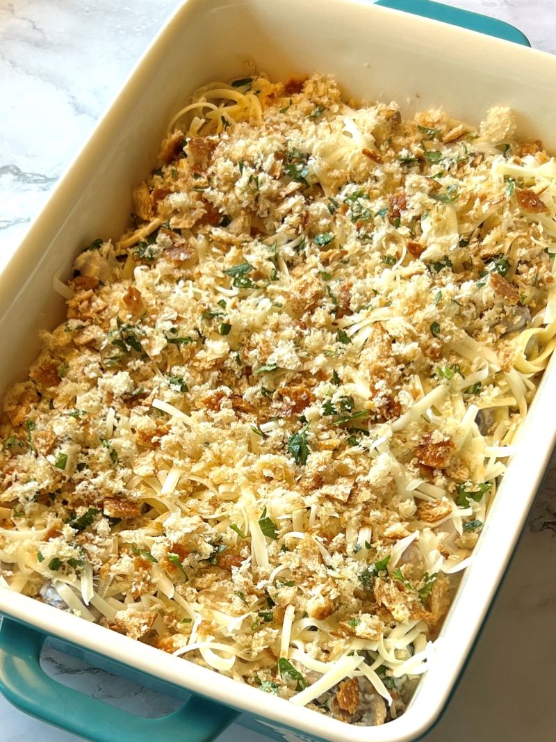 Tuna noodle mixture in a casserole dish topped with cheese and breadcrumbs. 