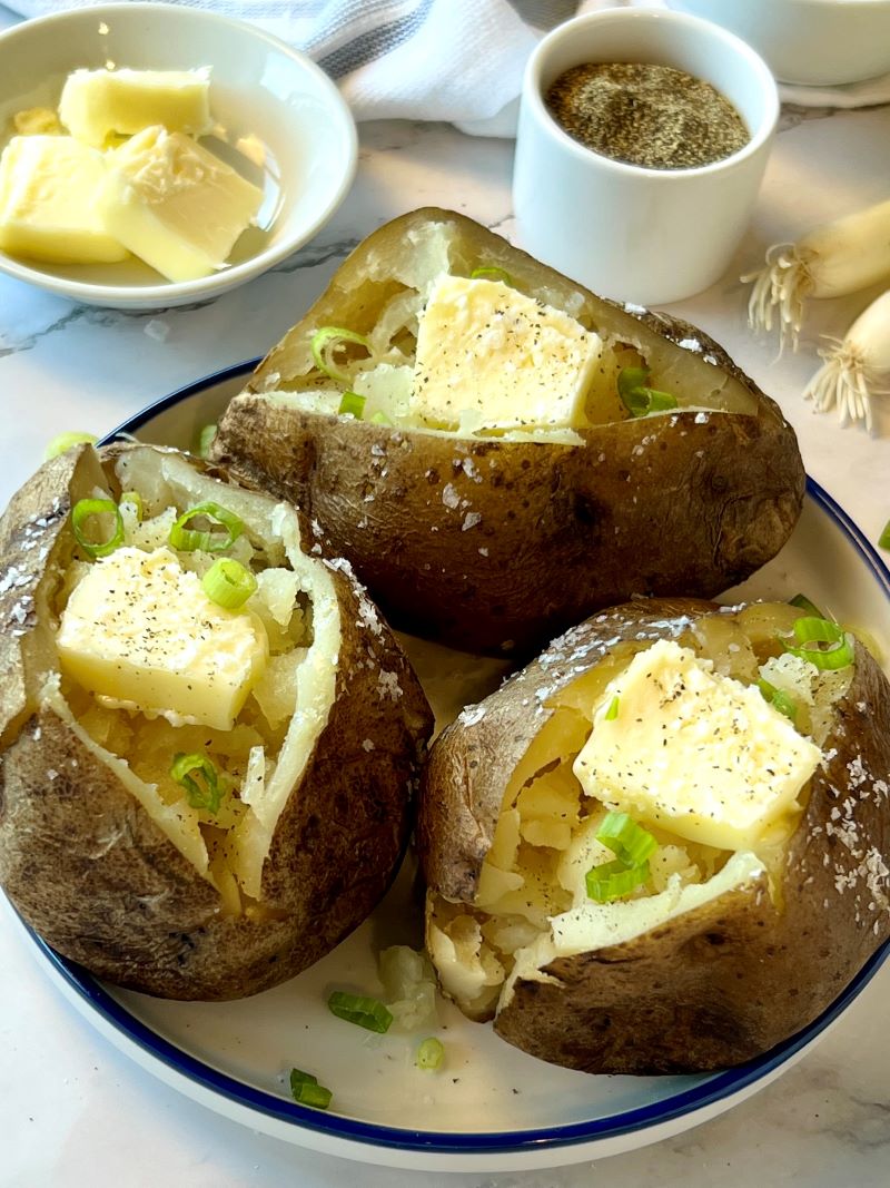 3 baked potatoes cut open with butter, salt, pepper, and green onion slices. 