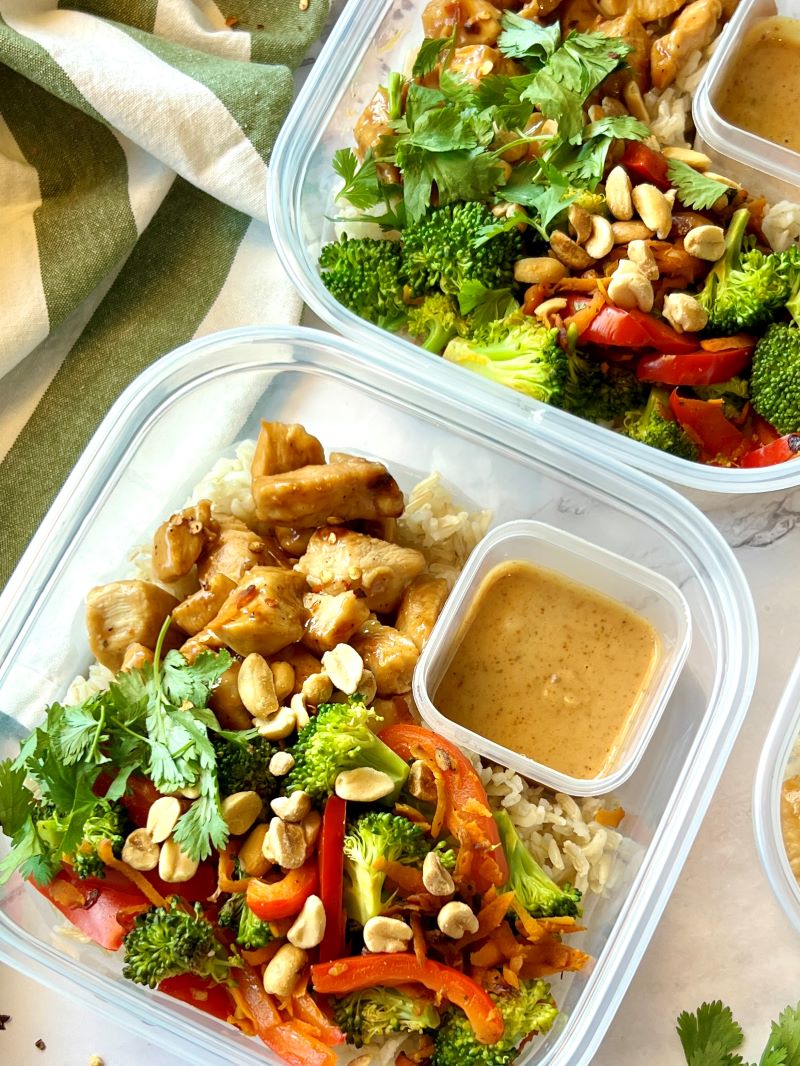 Thai chicken rice bowls assemble in meal prep containers with peanut sauce. 