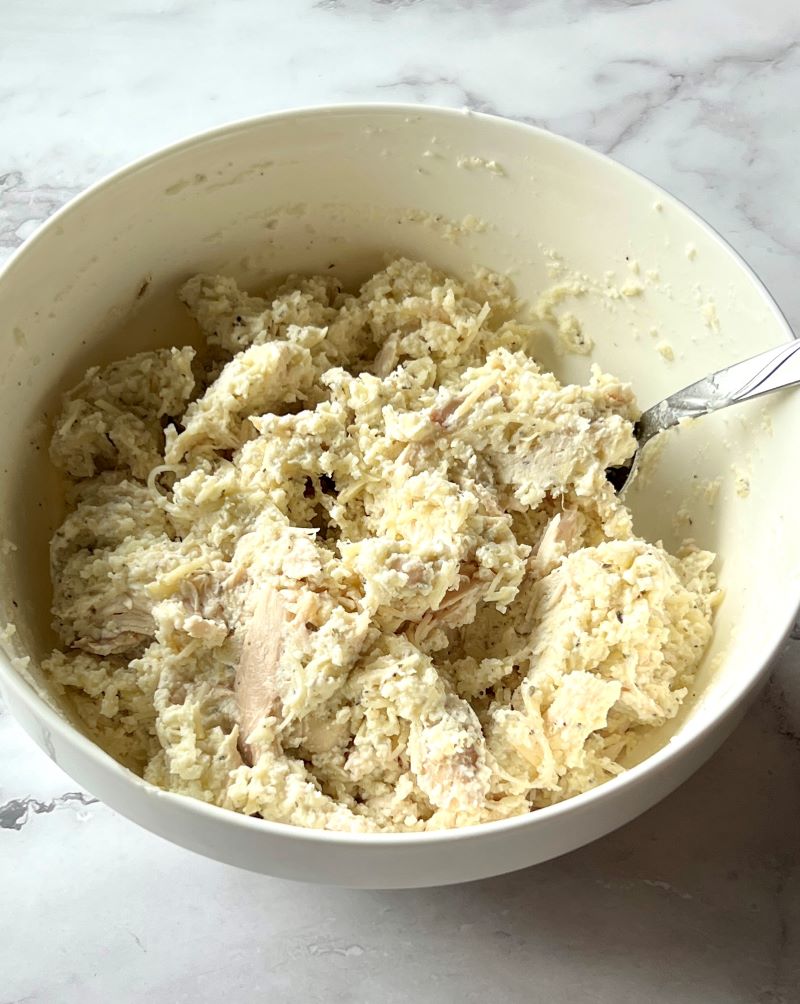 Chicken, cheese, and seasonings mixed in a medium bowl.