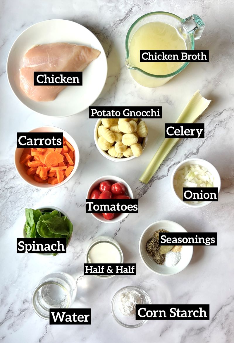Ingredients displayed for slow cooker chicken gnocchi soup. Chicken breast, chicken broth, potato gnocchi, carrots, celery, onions, tomatoes, spinach, seasonings, half and half, corn starch, and water.