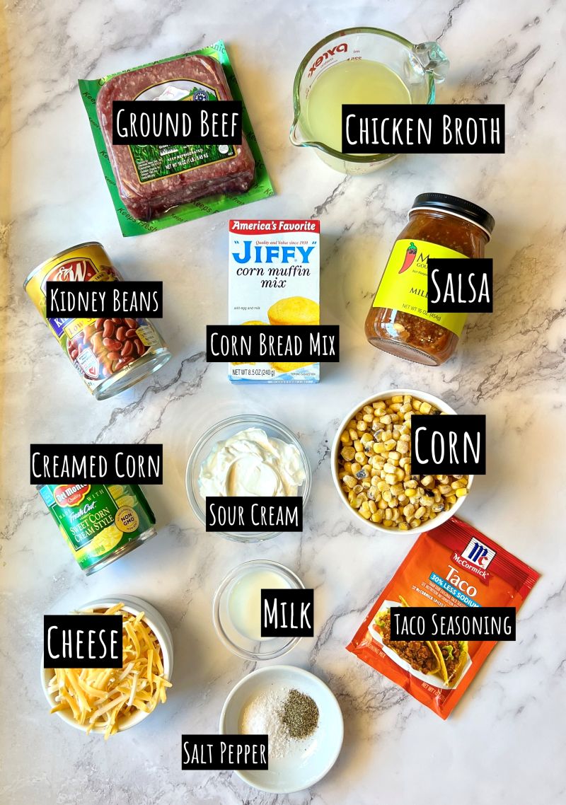 Ingredients displayed for cowboy cornbread casserole. Ground beef, chicken broth, jiffy cornbread mix, salsa, kidney beans, roasted corn, sour cream, creamed corn, milk, taco seasoning, cheese, salt and pepper.