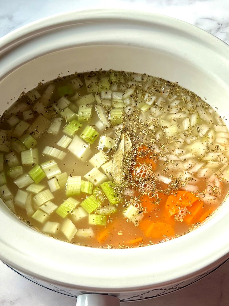 Chicken, veggies, seasonings and broth combined in a slow cooker.