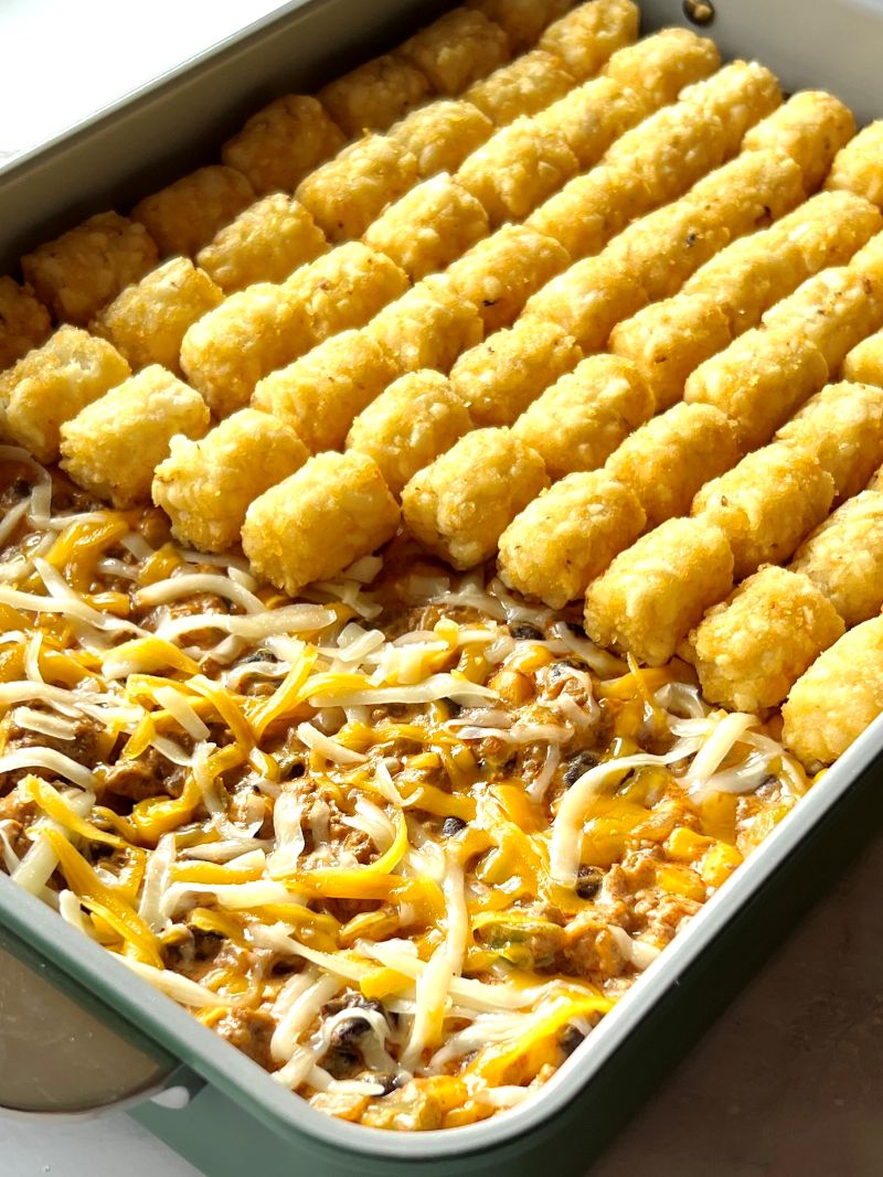 Tater tots placed on top of ground beef filling in a baking dish. 