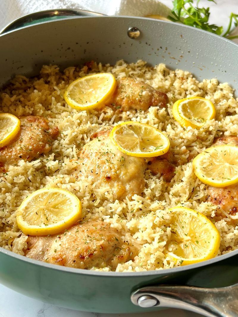 Skillet with cooked rice chicken, and lemon slices.