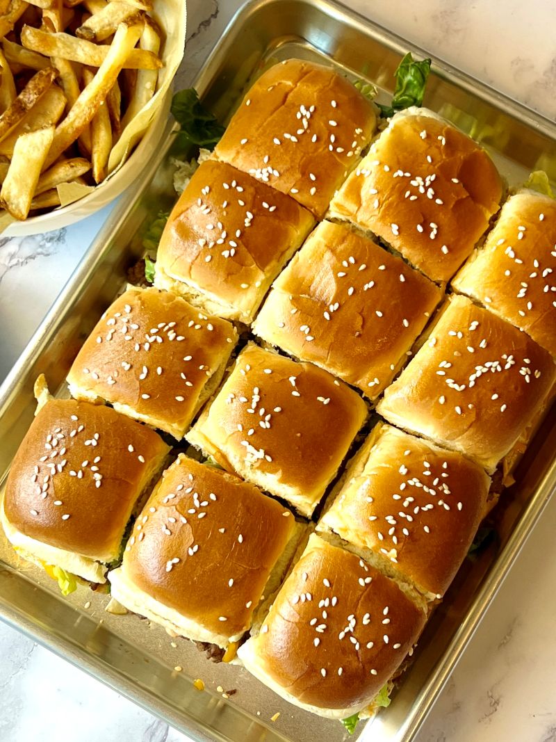 Sliders baked with top bun on a sheet pan with a side of baked French fries.