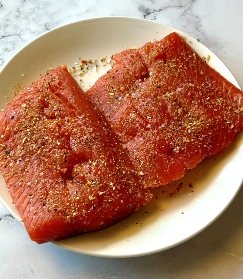 Raw salmon filets seasoned with lemon pepper and salt.