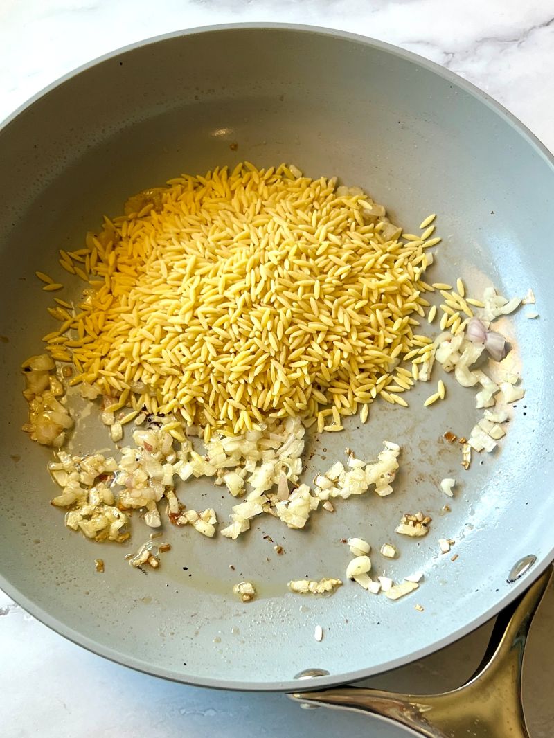 Orzo and shallots in a skillet.
