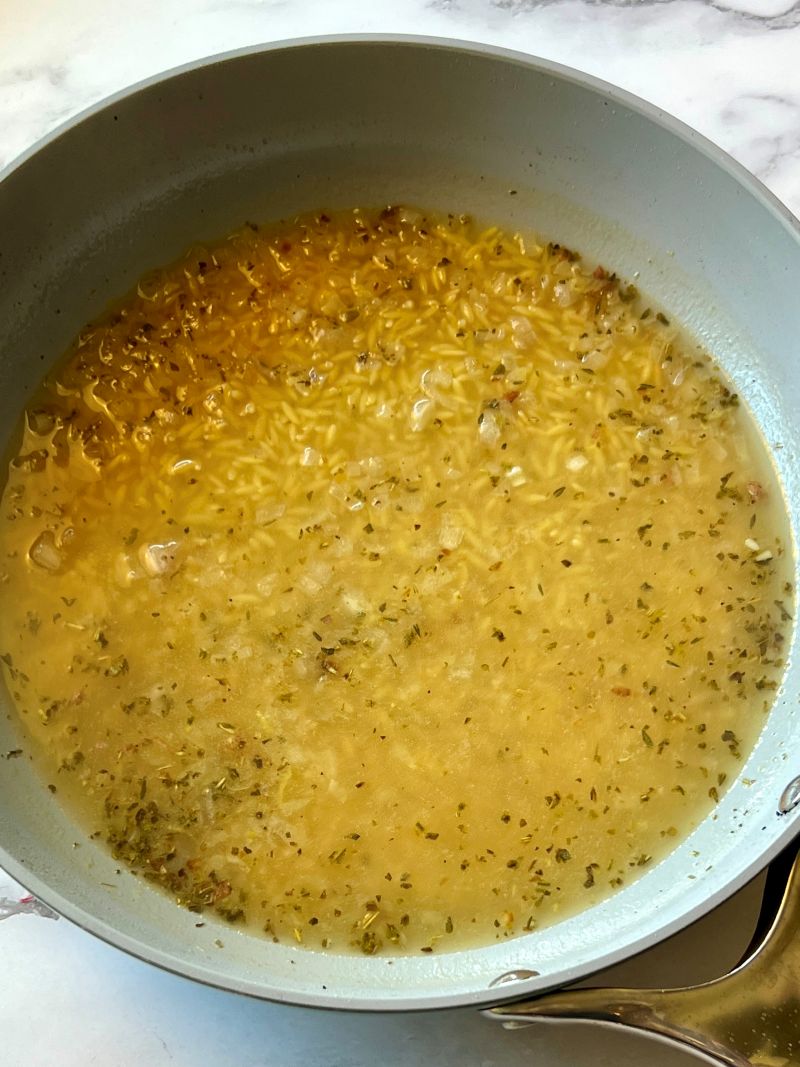 Broth mixed with orzo in a skillet. 