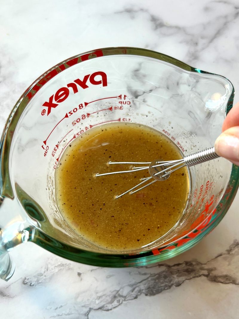 Dressing ingredients combined in a mixing bowl with a whisk.
